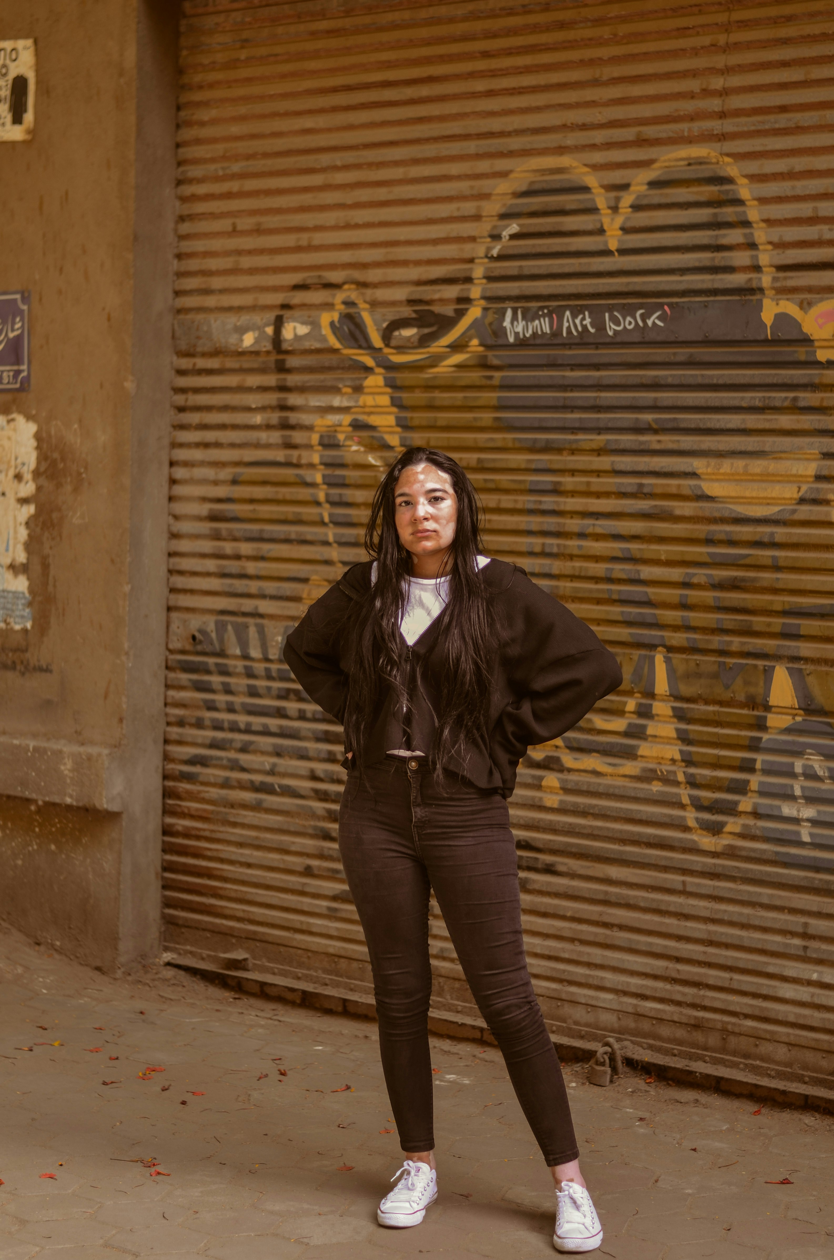 woman in black jacket and blue denim jeans standing beside brown wooden wall during daytime